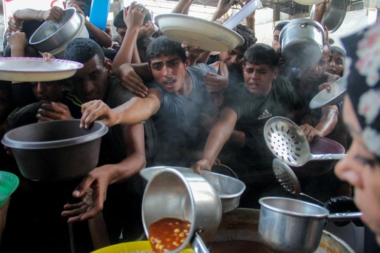 Young boys holding pots and bowls reach their arms for food.