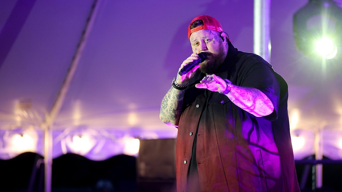 Country singer Jelly Roll wears backwards red hat on stage.