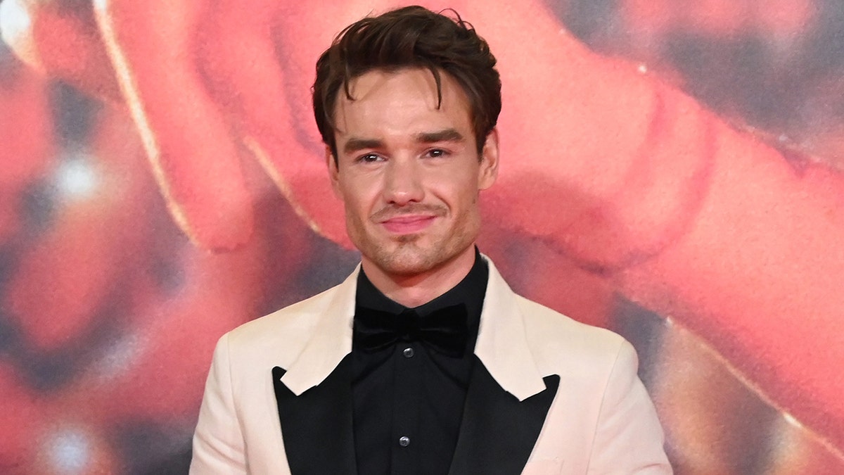 Liam Payne wears white suit with black shirt.