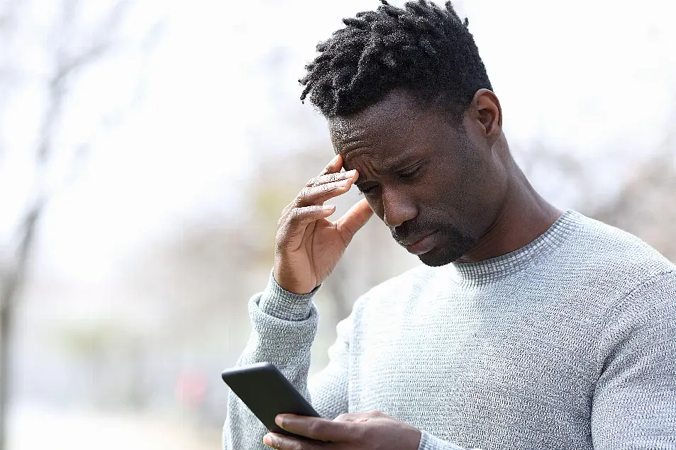 Stressed young man reading bad news on his phone while standing in a park 