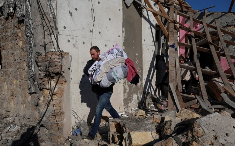 A person carries clothing as they navigate through the rubble of a destroyed building.