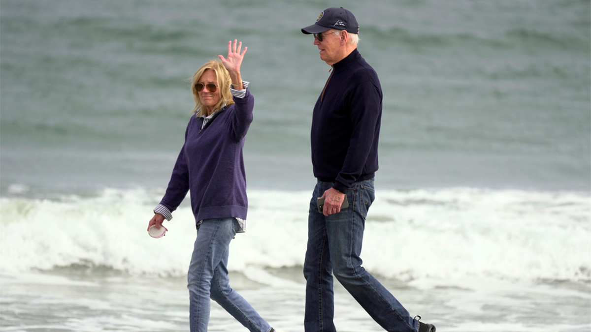 Jill Biden waving while walking on the beach with President Biden