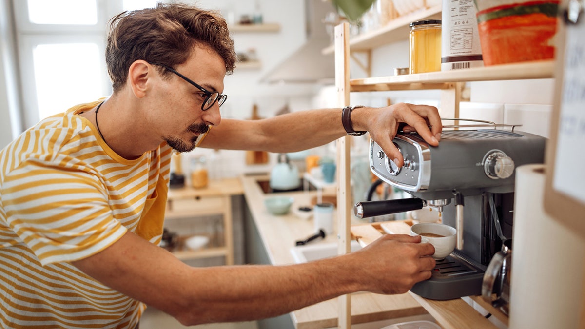 Young casually clothed man making coffee in his kitchen.