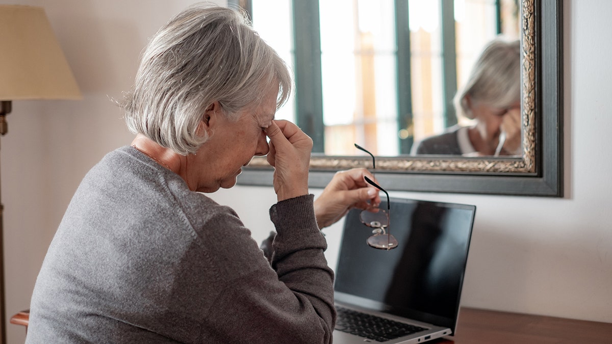 Tired woman touches her nose sitting at a desk