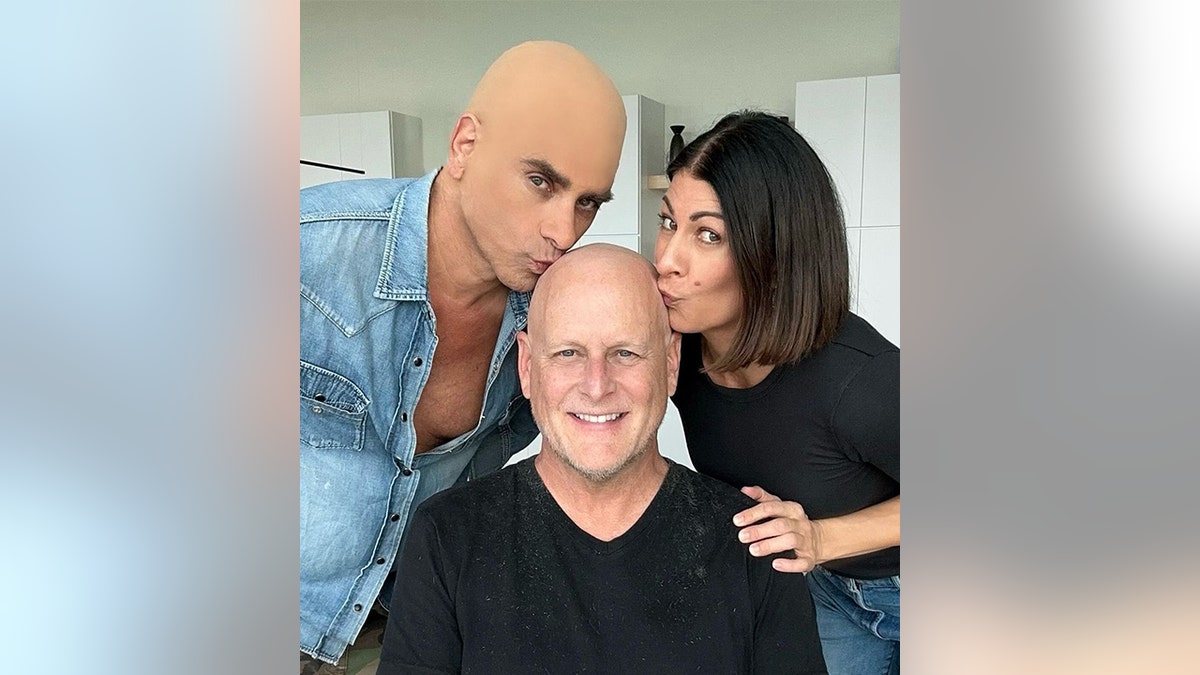 John Stamos in a bald cap and jean shirt kisses Dave Coulier's bald head, as does his wife Melissa